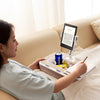 A woman is using a portable tablet stand to hold a phone and tablet while relaxing on a sofa.
