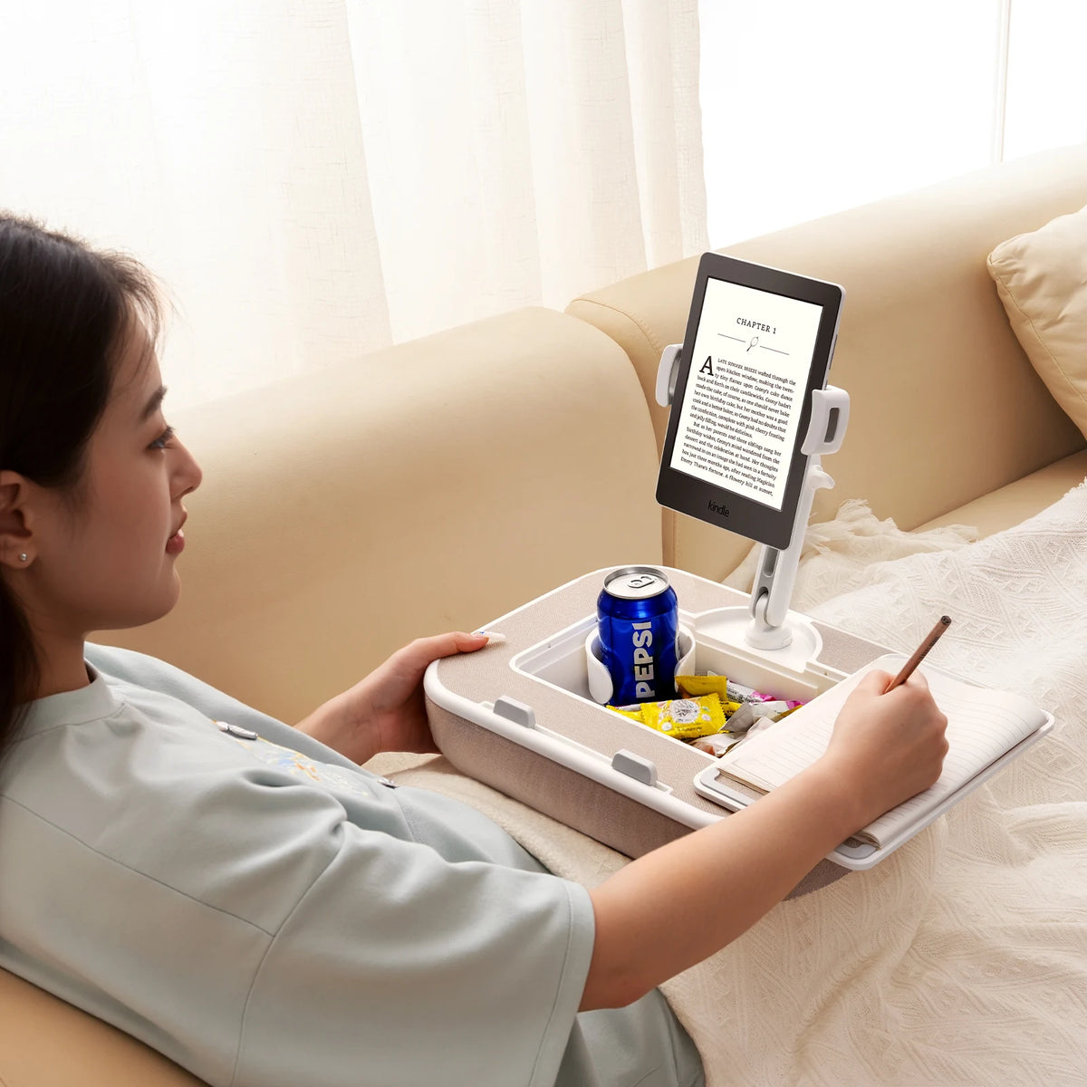 A woman is using a portable tablet stand to hold a phone and tablet while relaxing on a sofa.