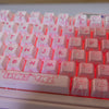 A close-up view of a translucent pink PBT keycap set for mechanical keyboards with various letter and number keys.