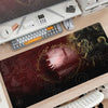 A large dark red gaming mouse pad featuring Lord of the Rings imagery placed on a wooden desk.