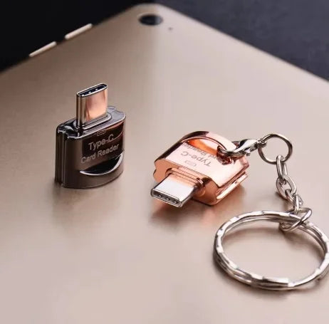 A gold-colored Type-C to Micro-SD card reader attached to a silver keyring, resting on a beige surface.