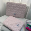 A pink quilted laptop sleeve is shown resting on a white surface.