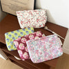 A collection of floral quilted ladies clutch purses in various pink, green, and red patterns are displayed on a wooden surfac