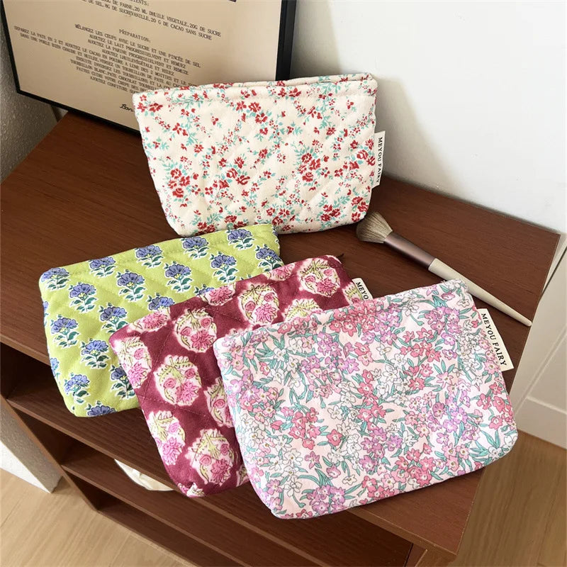A collection of floral quilted ladies clutch purses in various pink, green, and red patterns are displayed on a wooden surfac