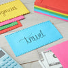 A collection of colorful envelopes, including yellow, pink, green, and blue, are displayed on a wooden surface next to a calc