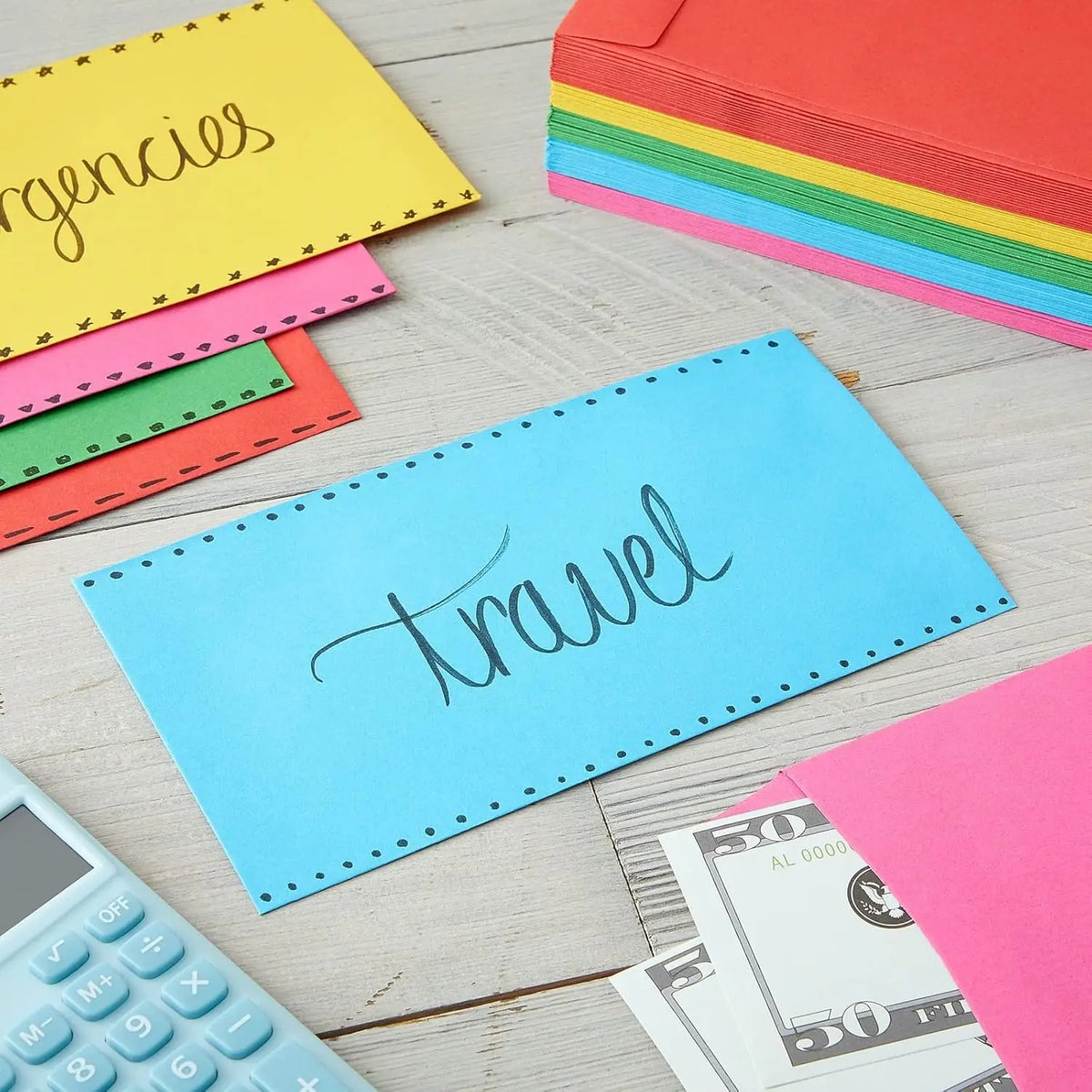 A collection of colorful envelopes, including yellow, pink, green, and blue, are displayed on a wooden surface next to a calc