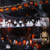 A dark Halloween scene featuring string lights, jack-o'-lantern decorations, and skeletal figures on a black surface.
