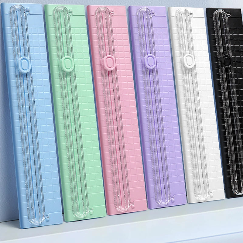A row of colorful portable manual paper cutters or trimmers in various shades including blue, green, pink, and purple.