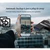 A hand holds an iPhone next to a SanDisk memory area backup device against a city skyline background.