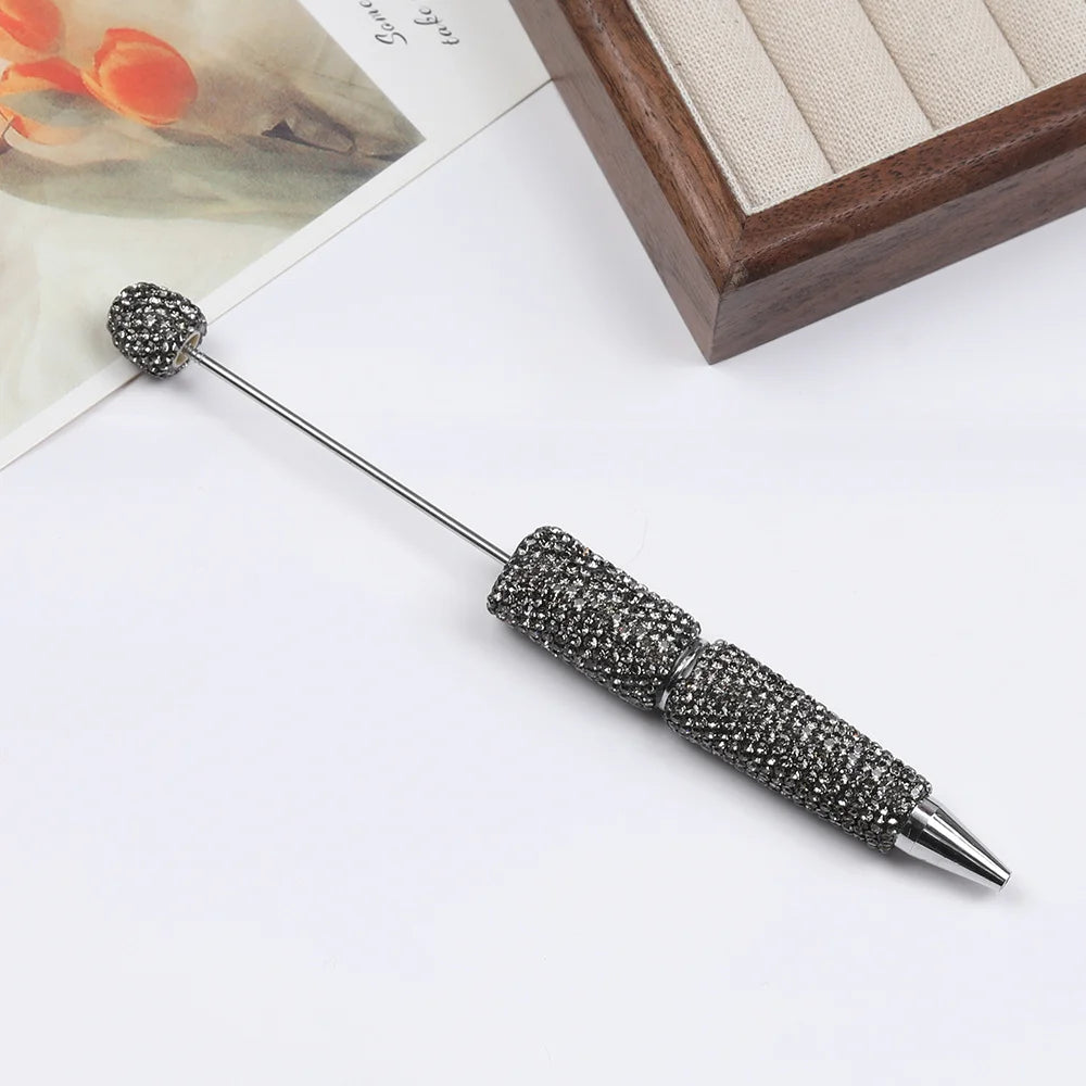 A silver pen accessory featuring a rhinestone beaded tip and a decorative sphere on a long metal shaft.