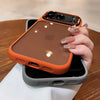 An orange clear shockproof case with camera lens protection for an iPhone is shown resting on a white surface.