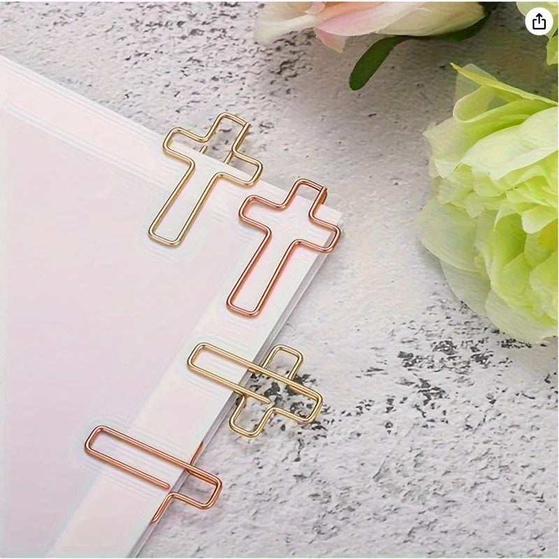 Gold tone decorative paper clips arranged on a white sheet of paper next to a light green flower.