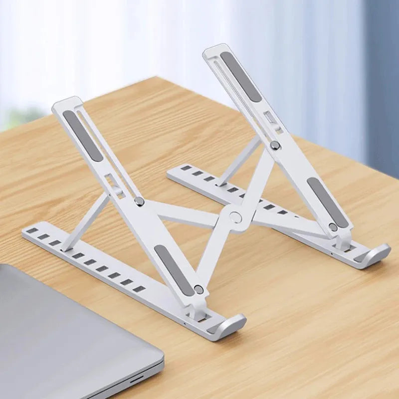 A white foldable adjustable laptop stand is shown resting on a wooden table.