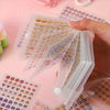 A hand is holding a clear storage book filled with numerous mini stickers featuring cute patterns for journaling and scrapboo