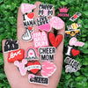A hand holds a collection of pink and black heart-shaped and text-based shoe charms for a personalized gift set.