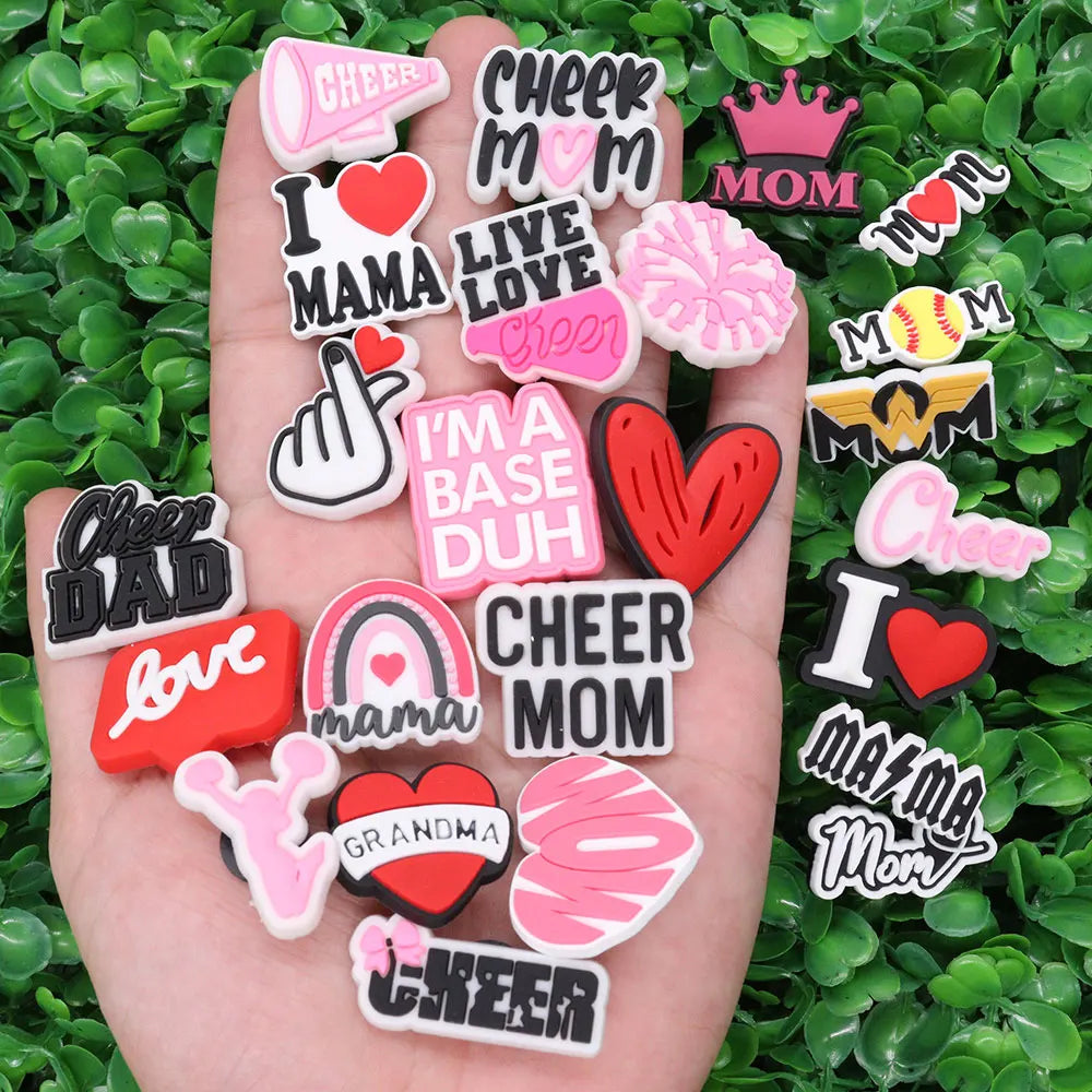 A hand holds a collection of pink and black heart-shaped and text-based shoe charms for a personalized gift set.
