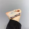 A hand holds a clear phone case with an orange tint for iPhone protection against a plain gray background.