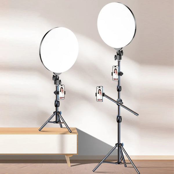 A white LED ring light with a tripod stand and boom arm is shown against a light gray wall.