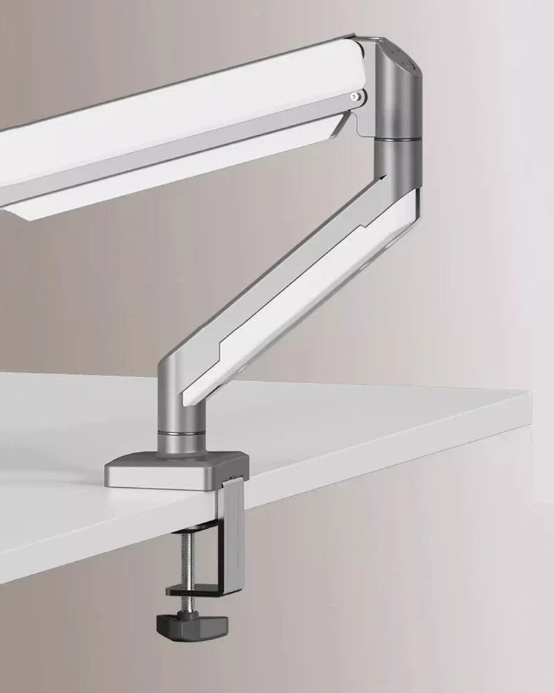 A silver adjustable desk monitor arm extending over a white desk surface.