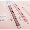 A pink plastic measuring tool shaped like a cat paw is shown next to a calendar and a ruler.