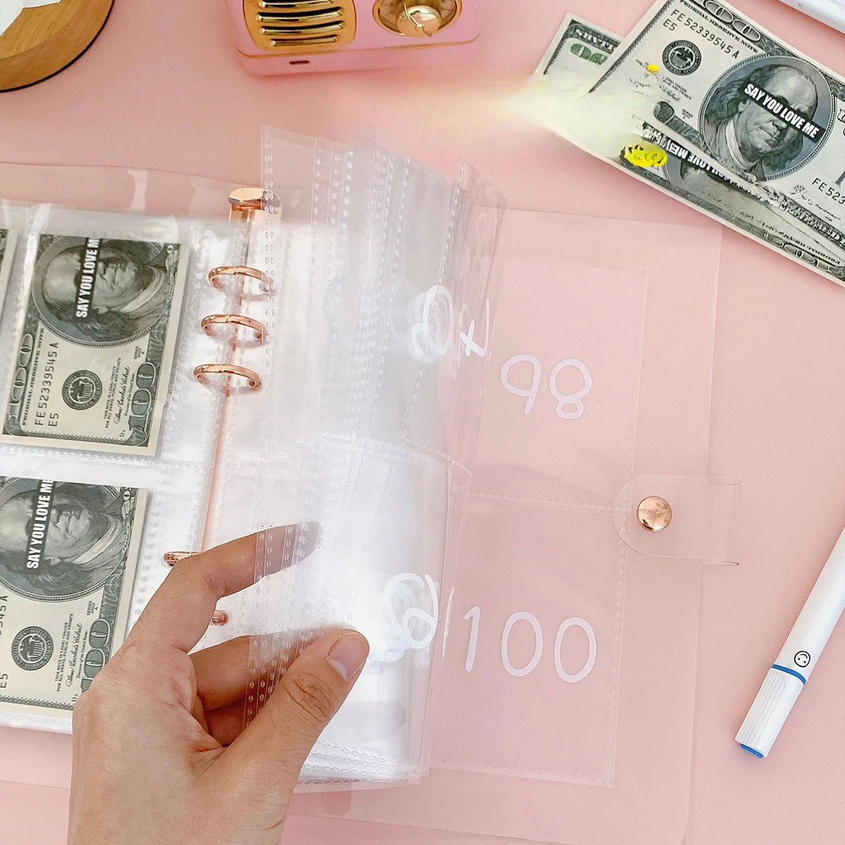 A hand is opening a clear pink envelope budget binder set for cash organization with US currency inside.