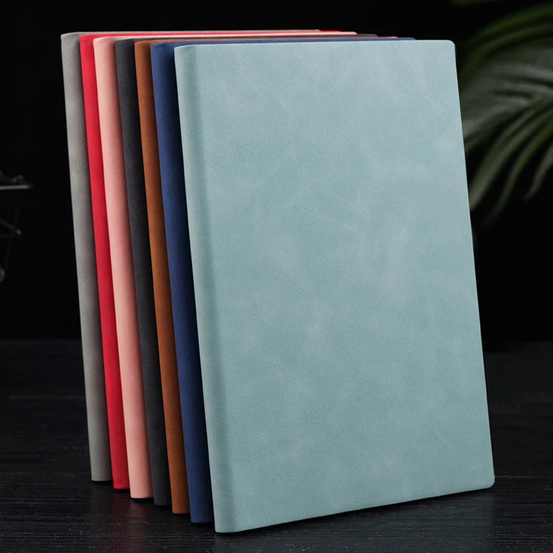 A stack of premium A5 leather journals in various muted colors, including blue-green and pink.