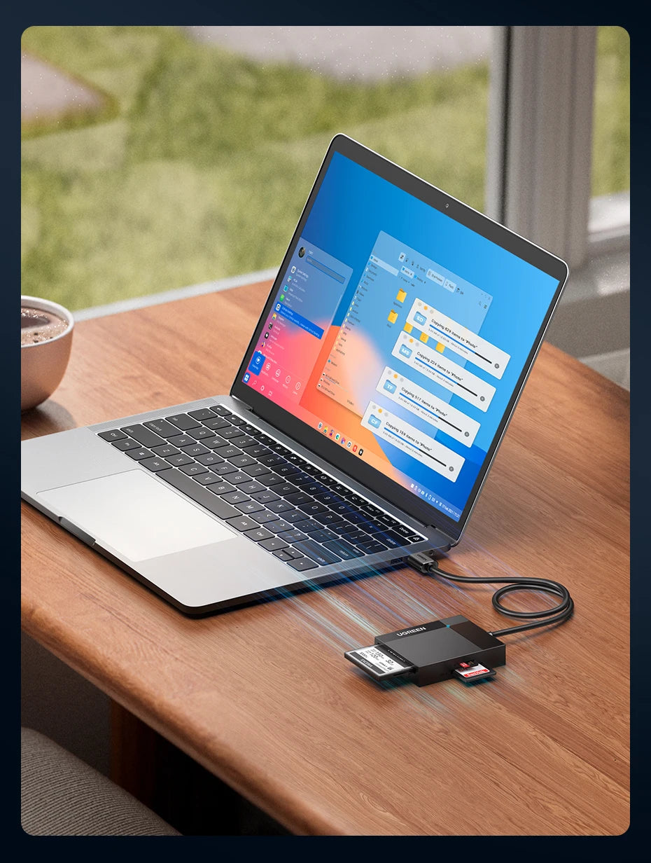 Una laptop plateada mostrando un adaptador de lector de tarjetas conectado a un cable negro sobre una mesa de madera.