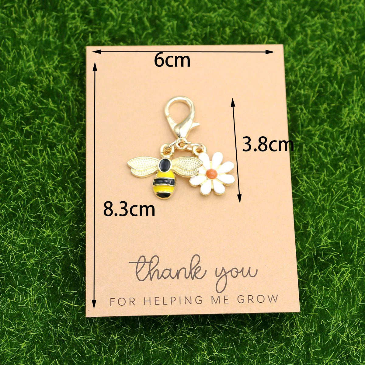 A thank you card with measurements and a ladybug and daisy keychain set displayed on green grass.