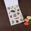 A white sticker book page featuring various fruit and accessory icons like a guitar, headphones, leather shoes, and various f