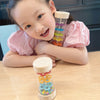 A young girl is holding a wooden rain sound tube musical instrument filled with colorful beads and other objects.