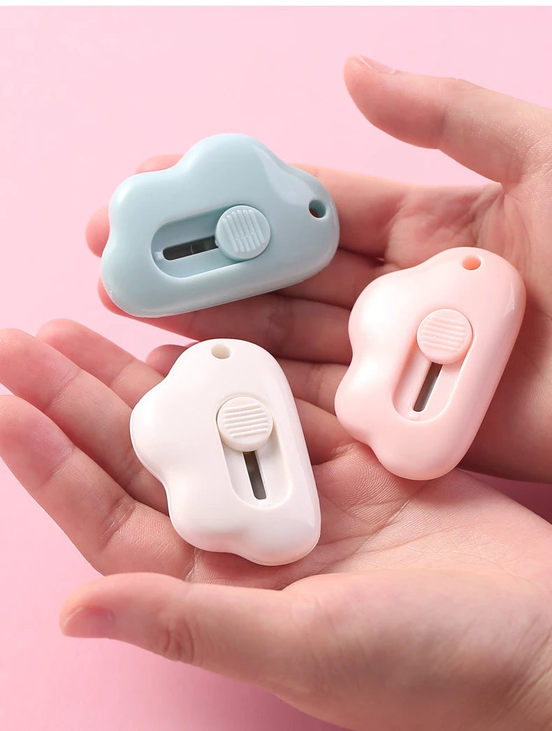 Two portable utility knives in light blue and pink are held in a person's hand.