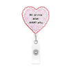 A pink heart-shaped badge reel with a scalloped edge and pink ribbon details, featuring the text BE SO FOR REAL RIGHT NOW.