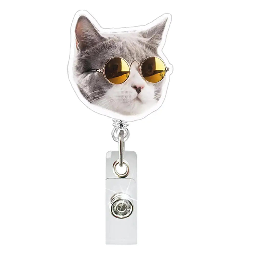A cat wearing round gold sunglasses is attached to a clear ID badge holder with a crocodile clip.