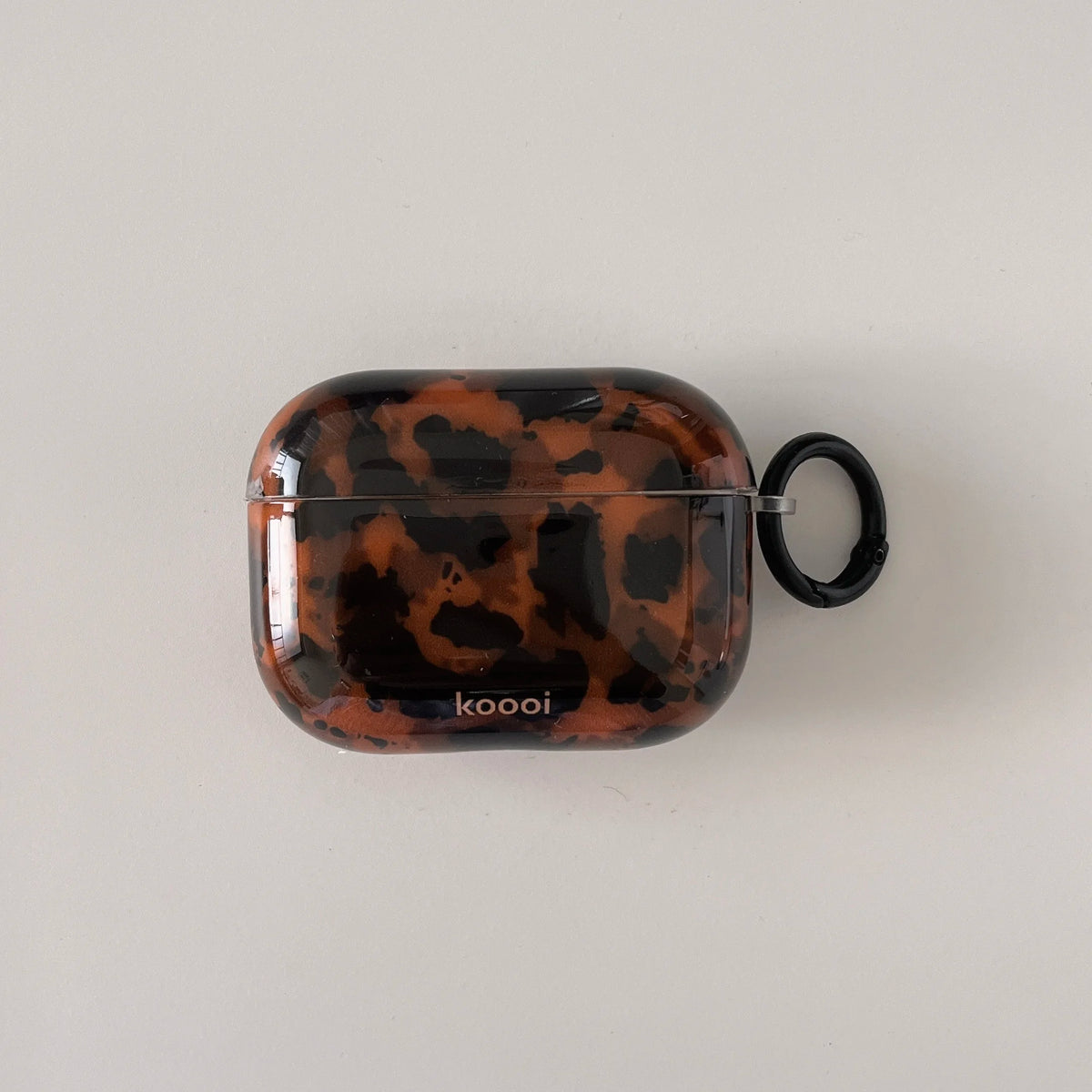 A glossy tortoiseshell patterned protective case for AirPods is shown against a white background.