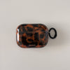 A glossy tortoiseshell patterned protective case for AirPods is shown against a white background.