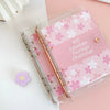 A pink A5 envelope budget binder set with gold hardware and floral patterns is displayed on a light surface.