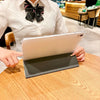 A person holds a silver tablet in a dark protective case on a wooden table.