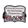 A lapel pin featuring a white enamel design with text and floral elements, titled Emotionally attached to fictional character