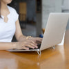 Una persona está usando un soporte portátil de laptop de aluminio en un escritorio de madera.