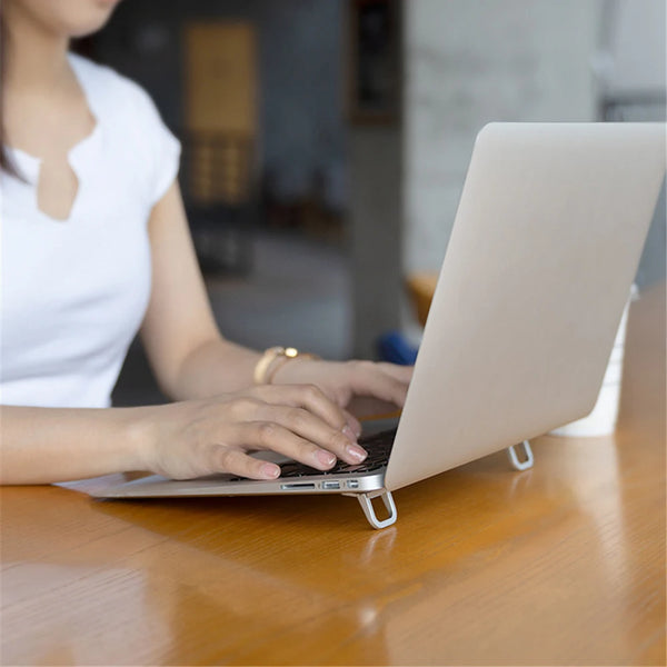 A person is using a portable aluminum laptop stand on a wooden desk.