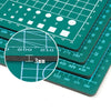 A close-up view of a green double-sided self-healing cutting mat with measurement lines and grid patterns.