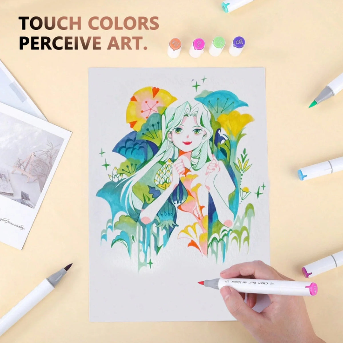 A hand holds an alcohol marker drawing a girl with vibrant colors on white paper surrounded by various colored markers.