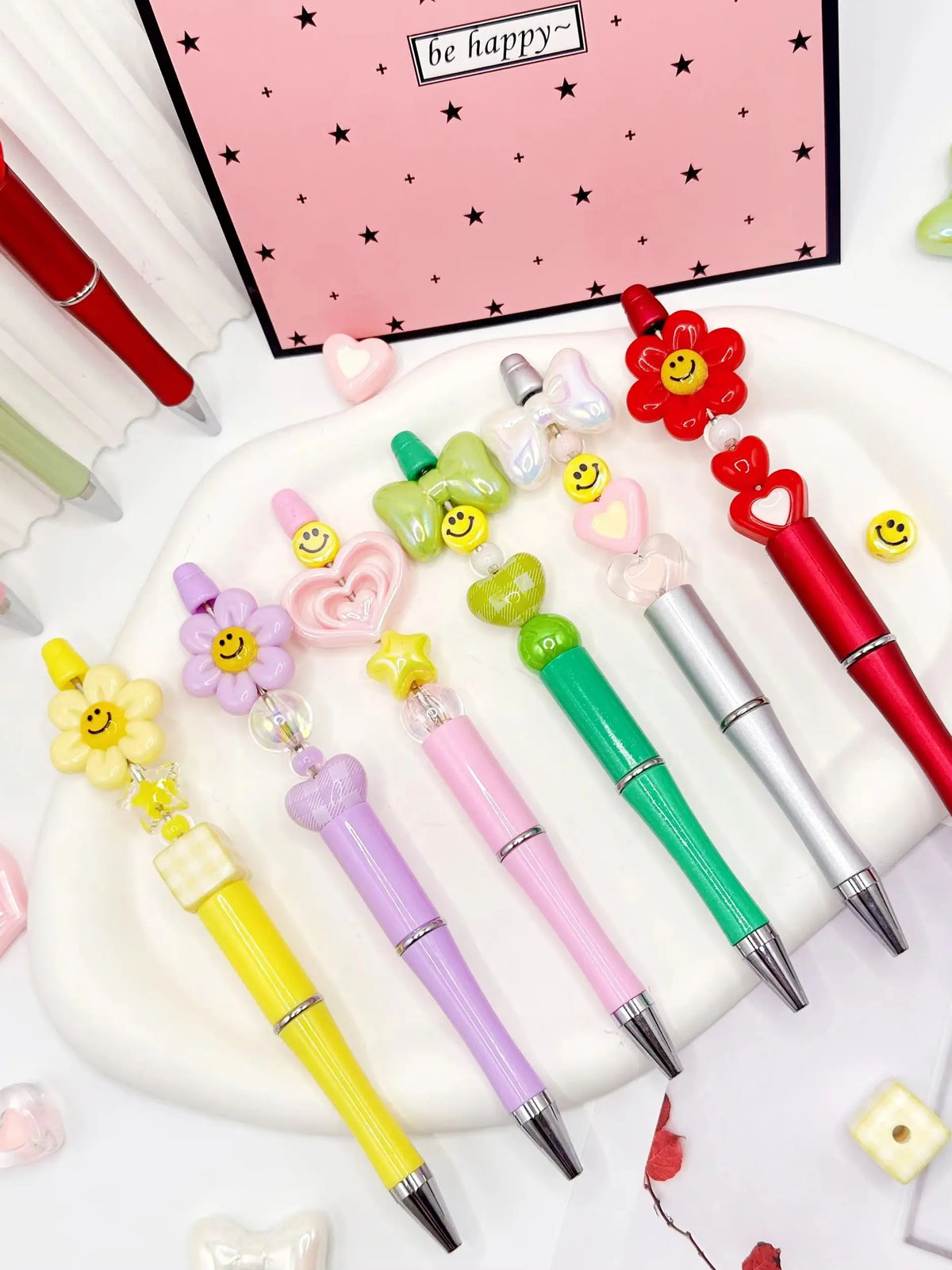 A set of colorful beaded ballpoint pens featuring pink, yellow, and green accents arranged on a white plate.