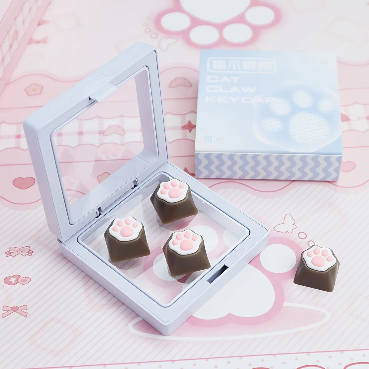 A clear plastic case holds several pink and brown cat paw keycaps for MX switches on a pink background.