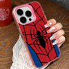 A hand holds a red and black spider web patterned phone case with a clear pink frame on a wooden surface.