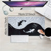 A gaming mouse pad featuring a black and white koi fish pattern placed on a wooden desk next to a laptop.