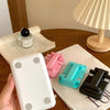 A hand holds a white adjustable foldable phone and tablet stand next to a stack of papers on a wooden table.