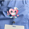 Pinkes herzförmiges Krankenschwester-Maskottchen mit Stethoskop an einer blauen Uniformtasche.