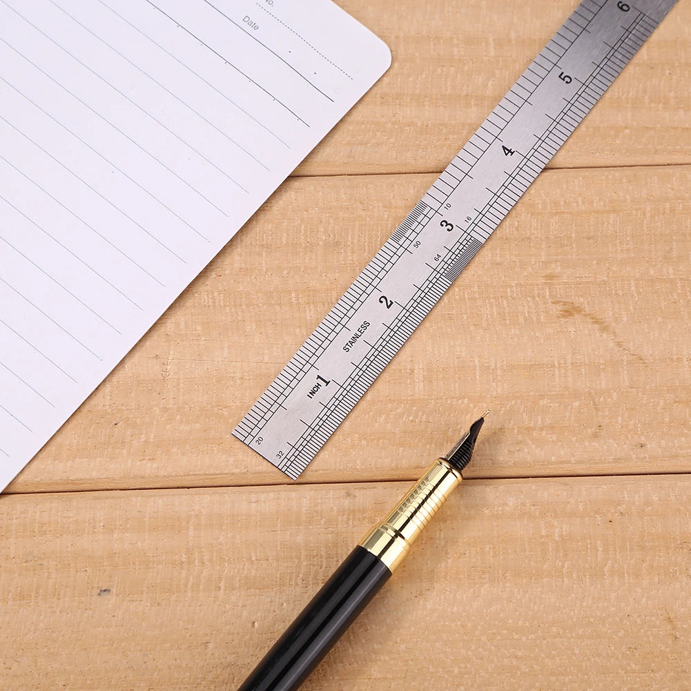 A black pen rests on a wooden surface next to a stainless steel measuring ruler and a sheet of paper.