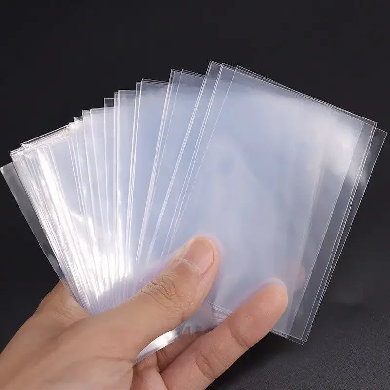 A hand holds a stack of clear protective sleeves for trading cards.